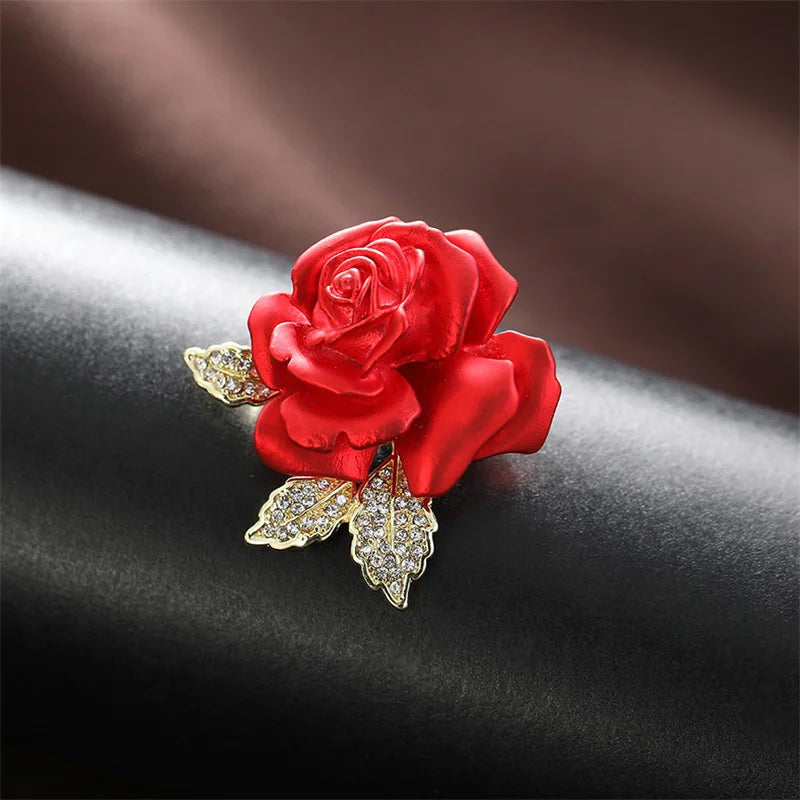 Red rose brooch with gold leaves on a dark surface