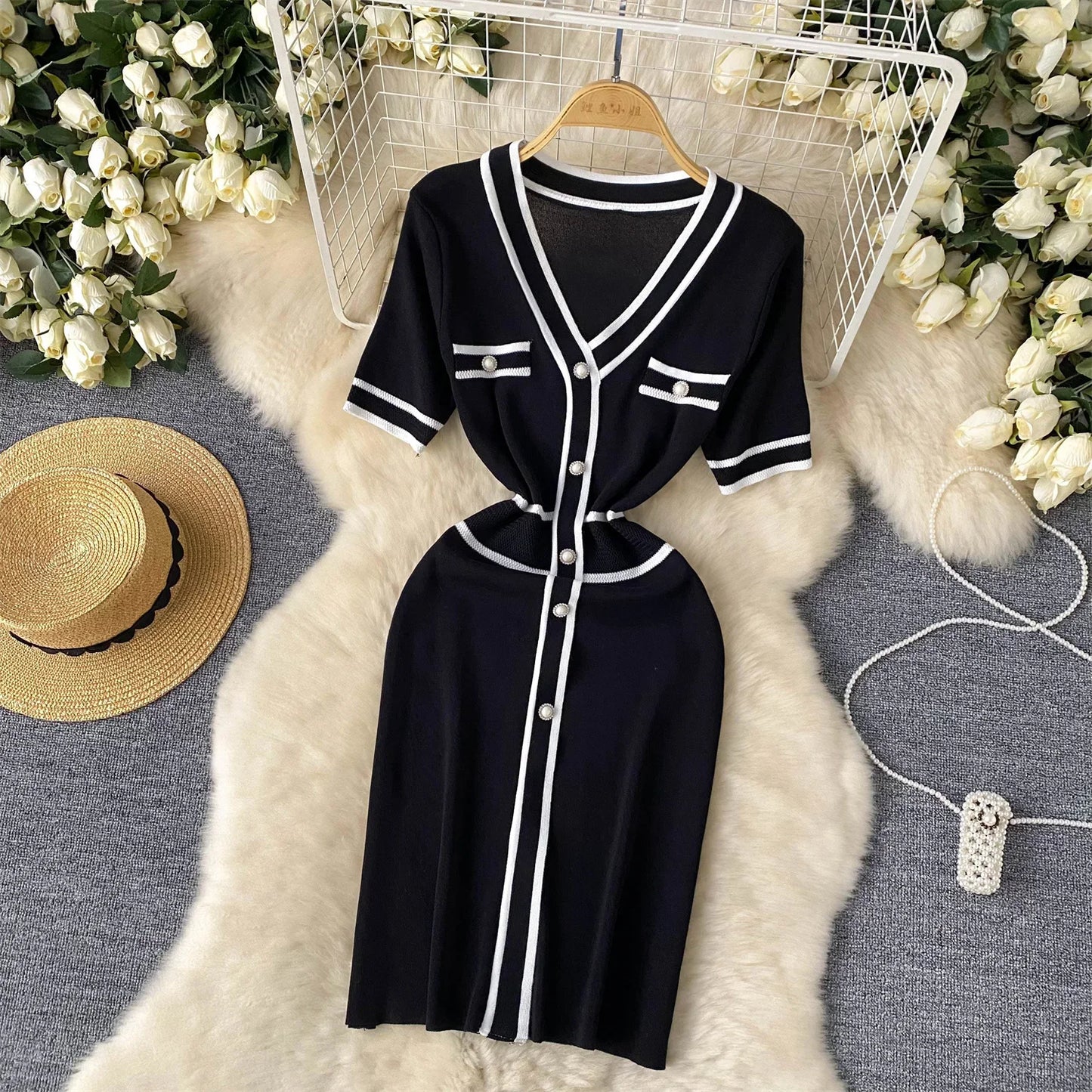 Black dress with White accents on a hanger surrounded by flowers and a hat.