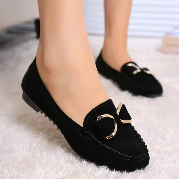Black loafers with gold accents worn on a White surface