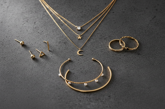 Delicate everyday jewelry collection featuring gold necklaces, stud earrings, simple rings and bracelets on a dark surface with soft dramatic lighting