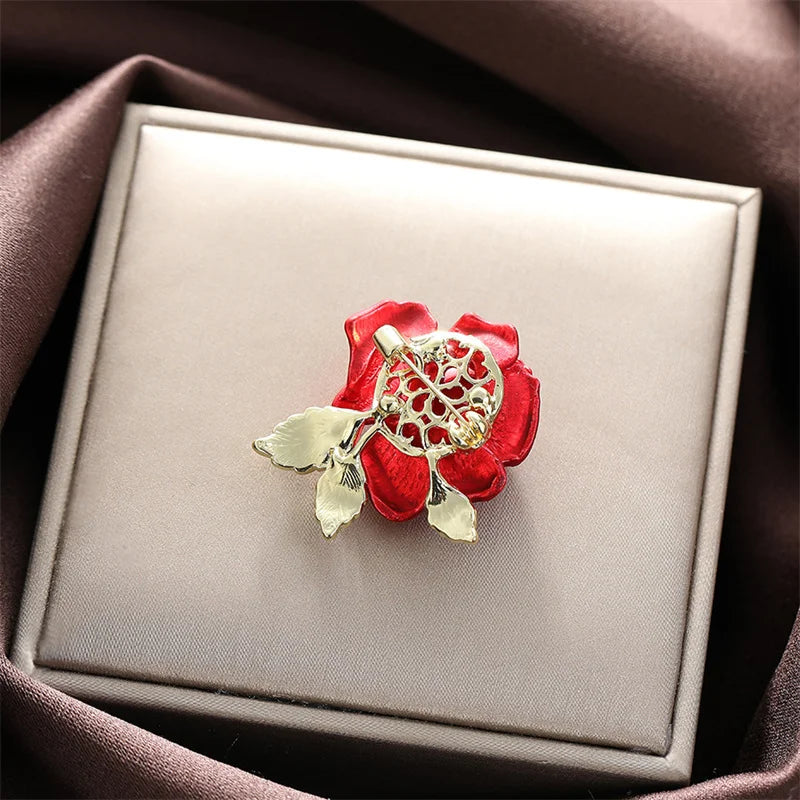 Red flower-shaped brooch with gold detailing on a beige jewelry box.