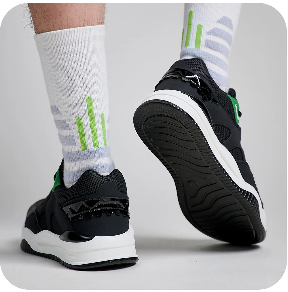 Black and White sneakers with Green accents worn with White socks featuring Green and Gray patterns on a light Gray background.