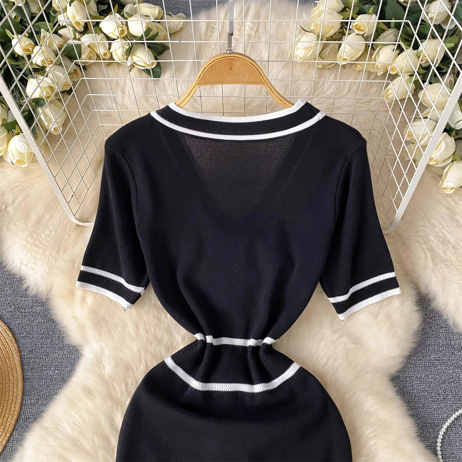 Black dress with White trim on a hanger against a decorative background with flowers.