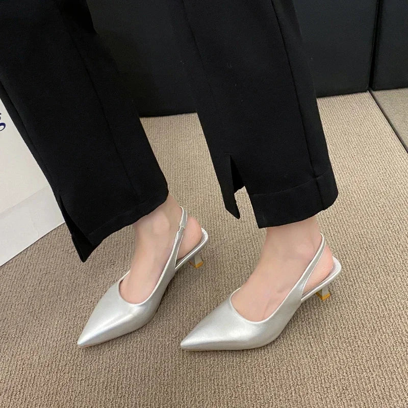Silver pointed-toe shoes worn with Black pants on a carpeted floor.