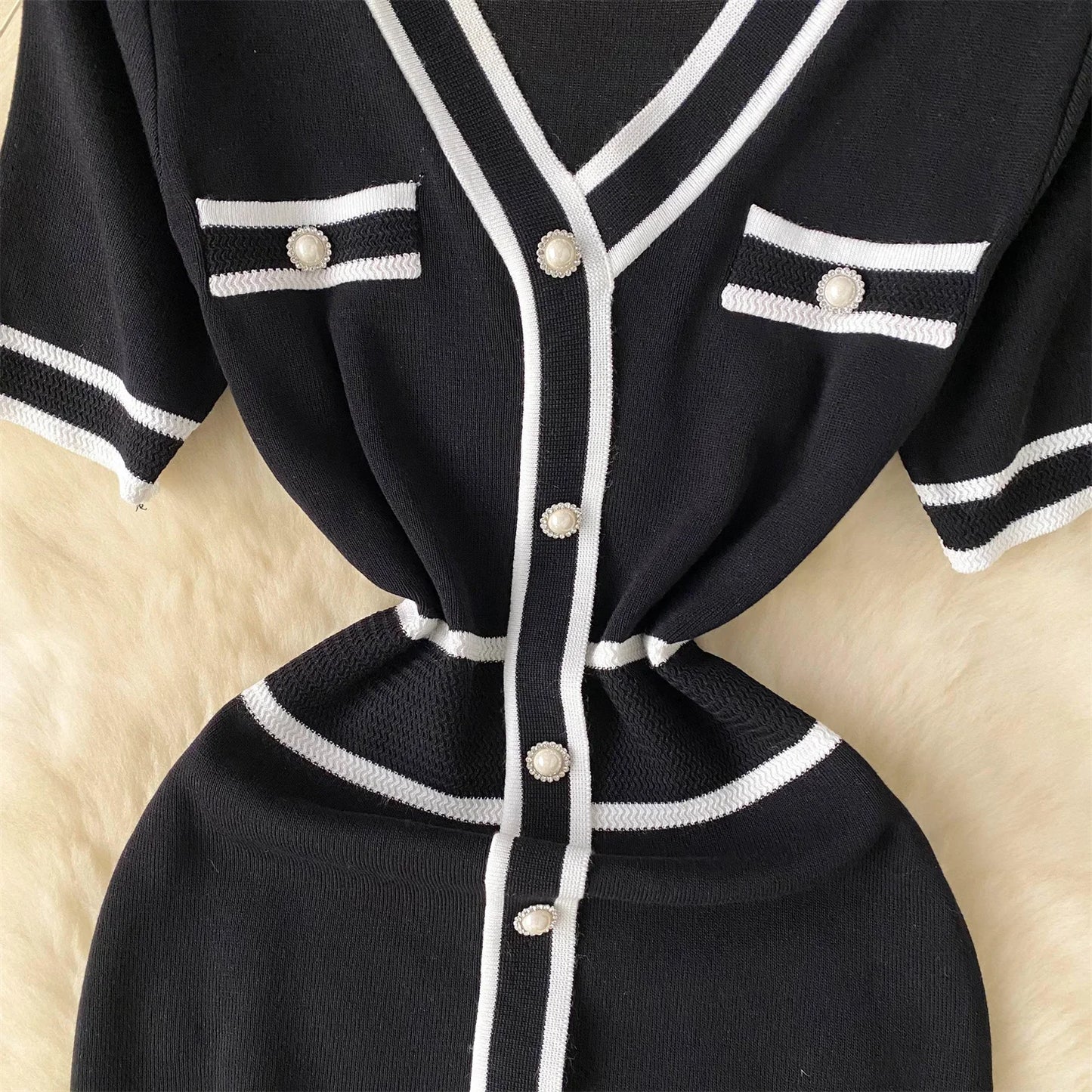 Black cardigan with White buttons and trim on a beige background
