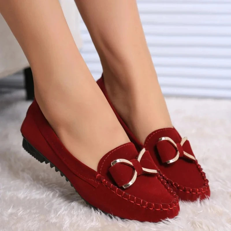 Red loafers with gold buckles worn by a person on a White surface.