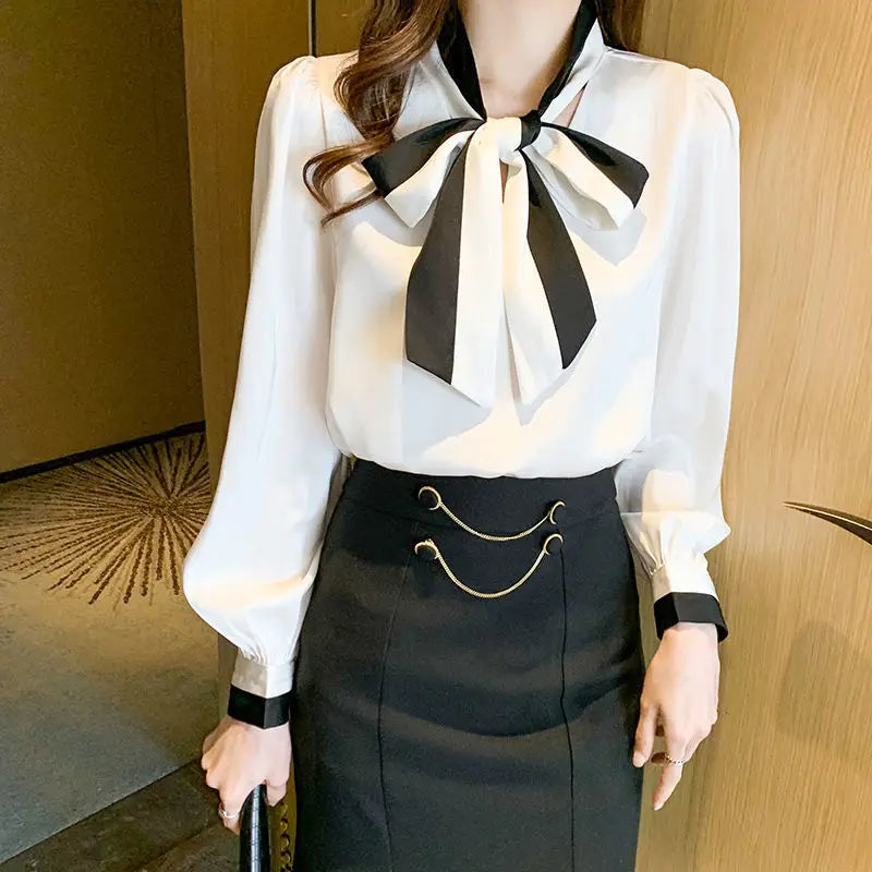 Person wearing a White blouse with a large Black bow and a Black skirt indoors.