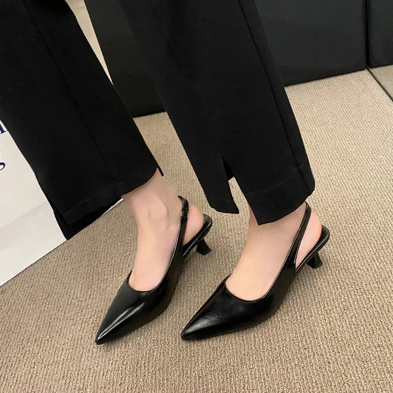 Black pointed-toe shoes worn with Black pants on a neutral background