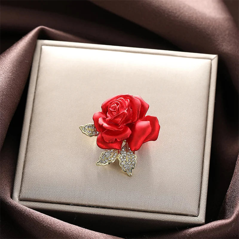 Red rose brooch with gold accents on a beige jewelry box