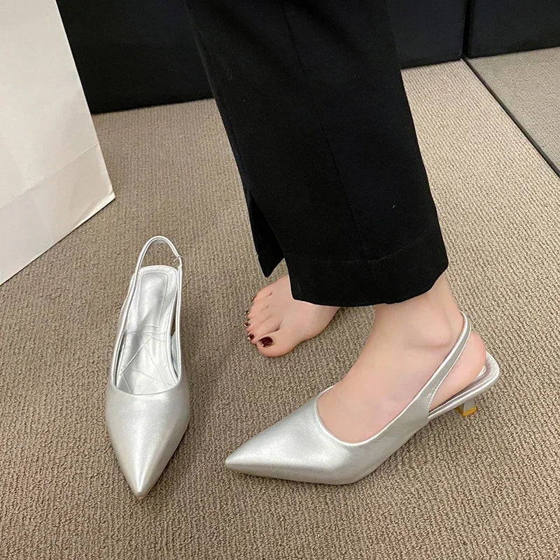 Silver pointed-toe shoes on a person wearing Black pants on a beige carpet.