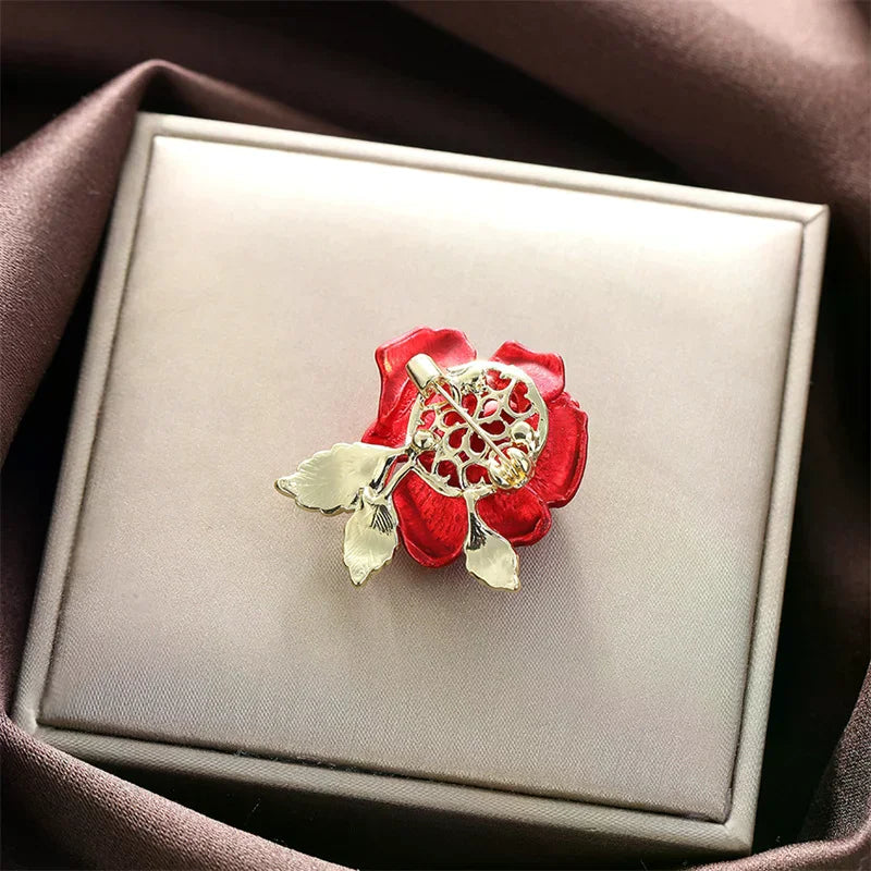 Red flower-shaped brooch with gold detailing on a Gray jewelry box.