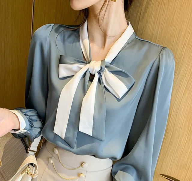 Person wearing a light Blue blouse with a large White bow tie against a wooden background