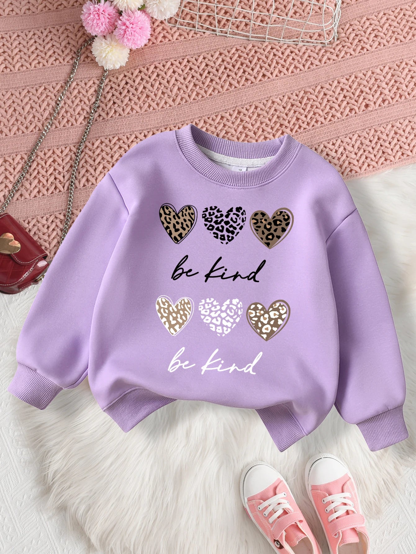 Purple sweatshirt with heart designs and 'be kind' text on a Pink textuRed surface.
