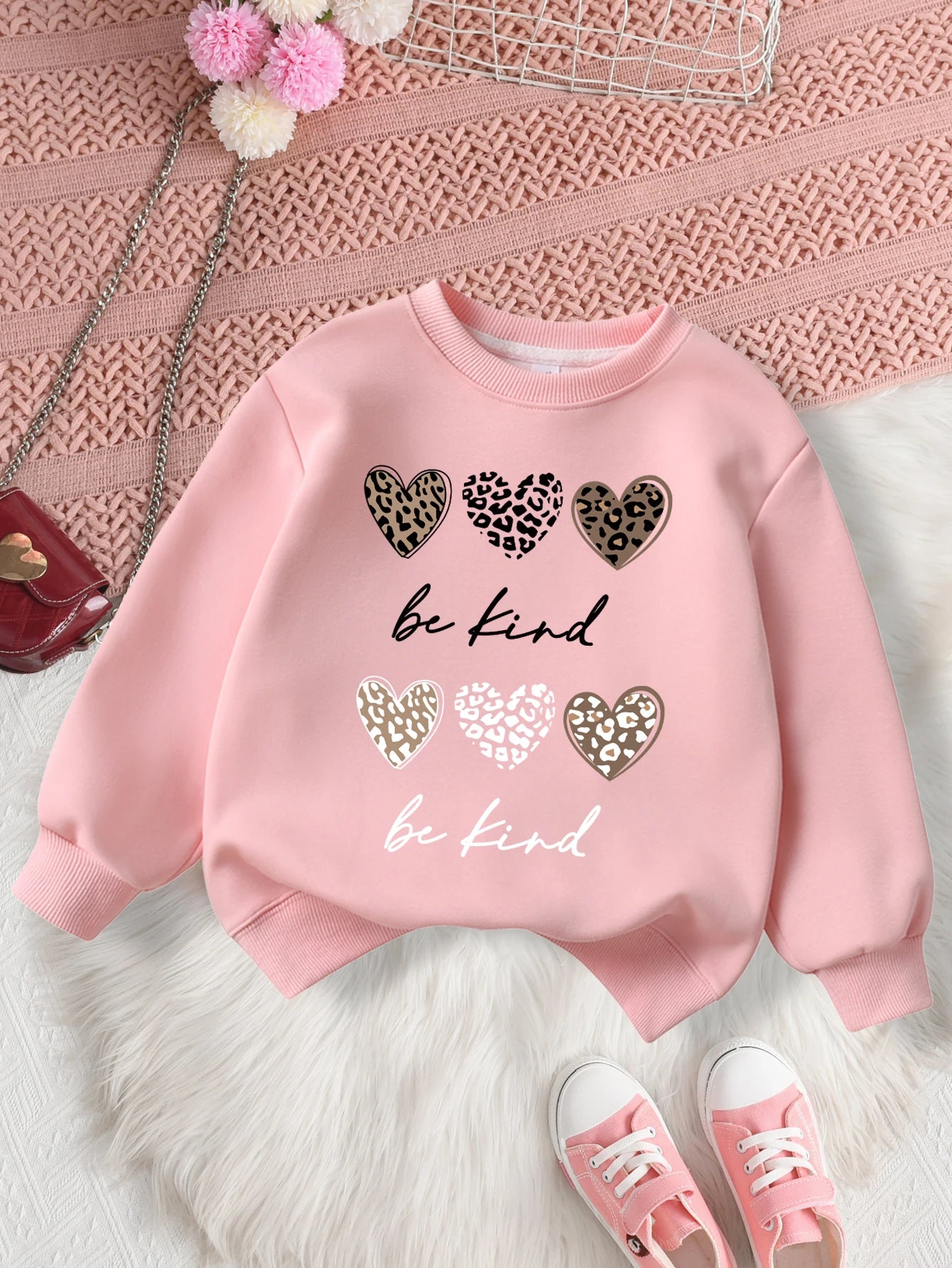Pink sweatshirt with heart designs and 'be kind' text on a textuRed surface.