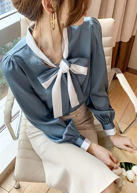 Person wearing a Blue blouse with a large bow tie sitting on a chair.