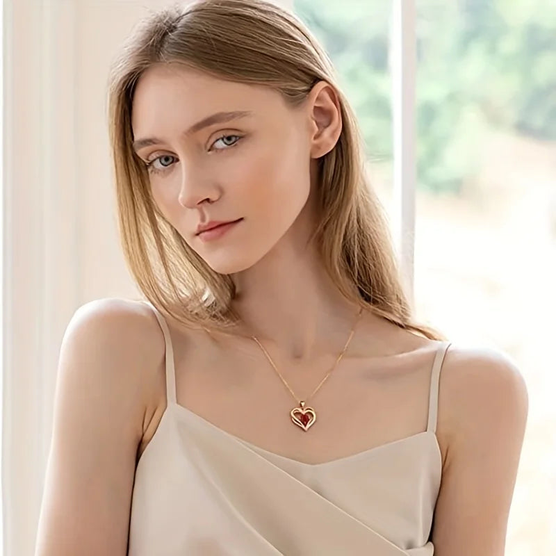 Woman wearing a gold necklace with a heart-shaped pendant in a softly lit room.