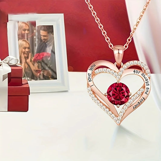 Heart-shaped gold necklace with a Red gemstone and engraved text, placed on a White surface with a Red background.