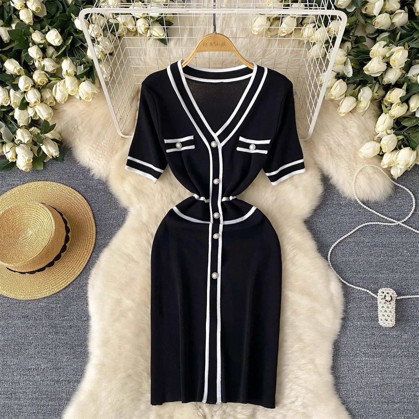 Black dress with White buttons on a hanger against a floral and textuRed background