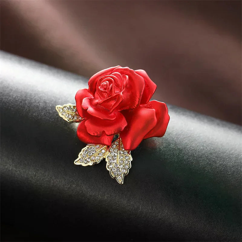 Red rose brooch with gold leaves on a dark fabric background