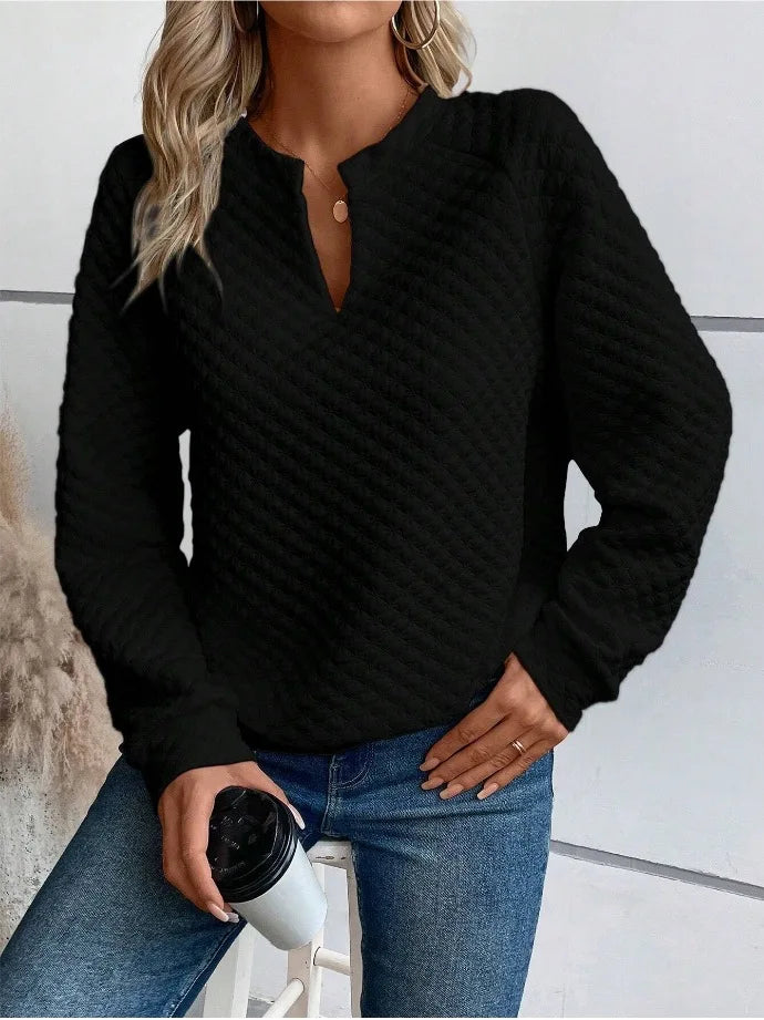 Person wearing a Black textuRed sweater holding a coffee cup against a neutral background