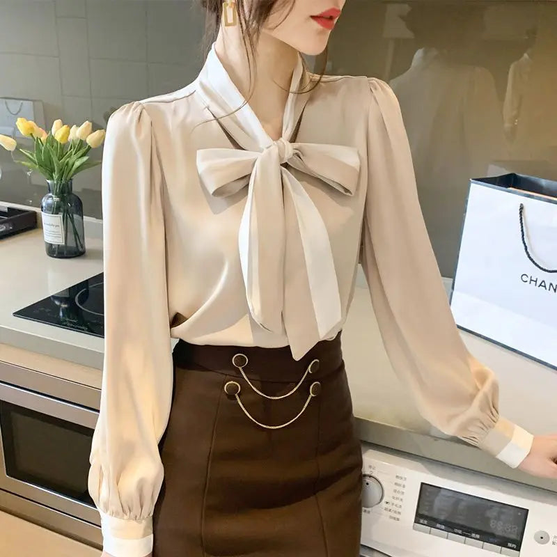 Woman wearing a beige blouse with a large bow tie in a kitchen setting.