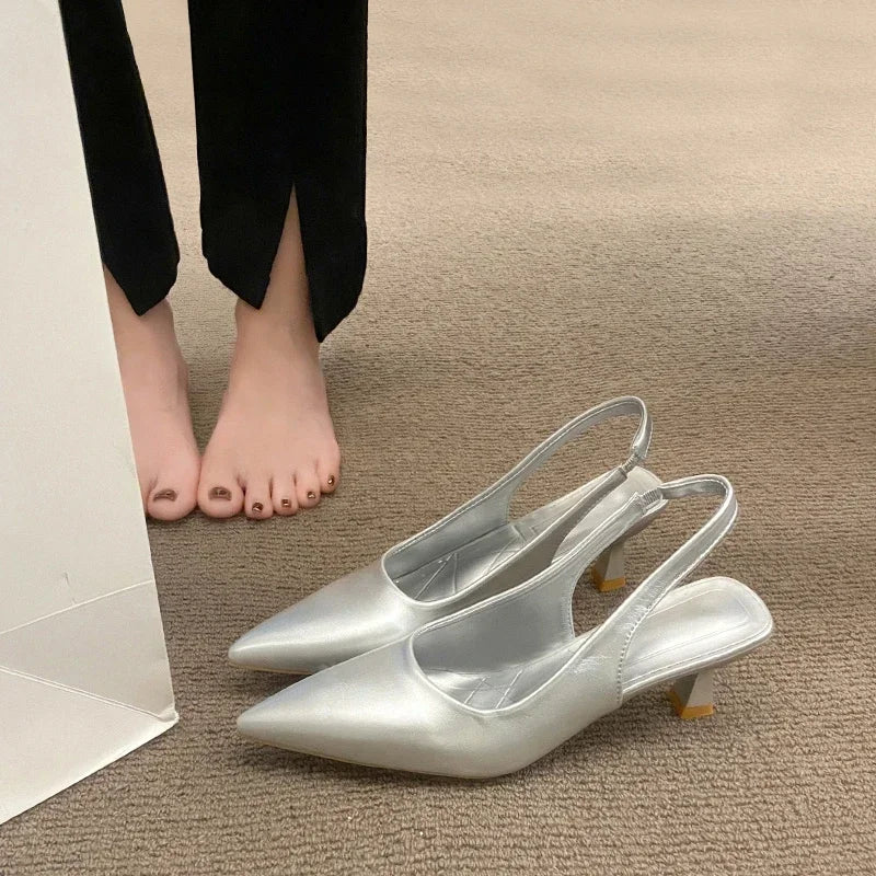 Silver high-heeled shoes on a beige carpet with a person wearing Black pants.