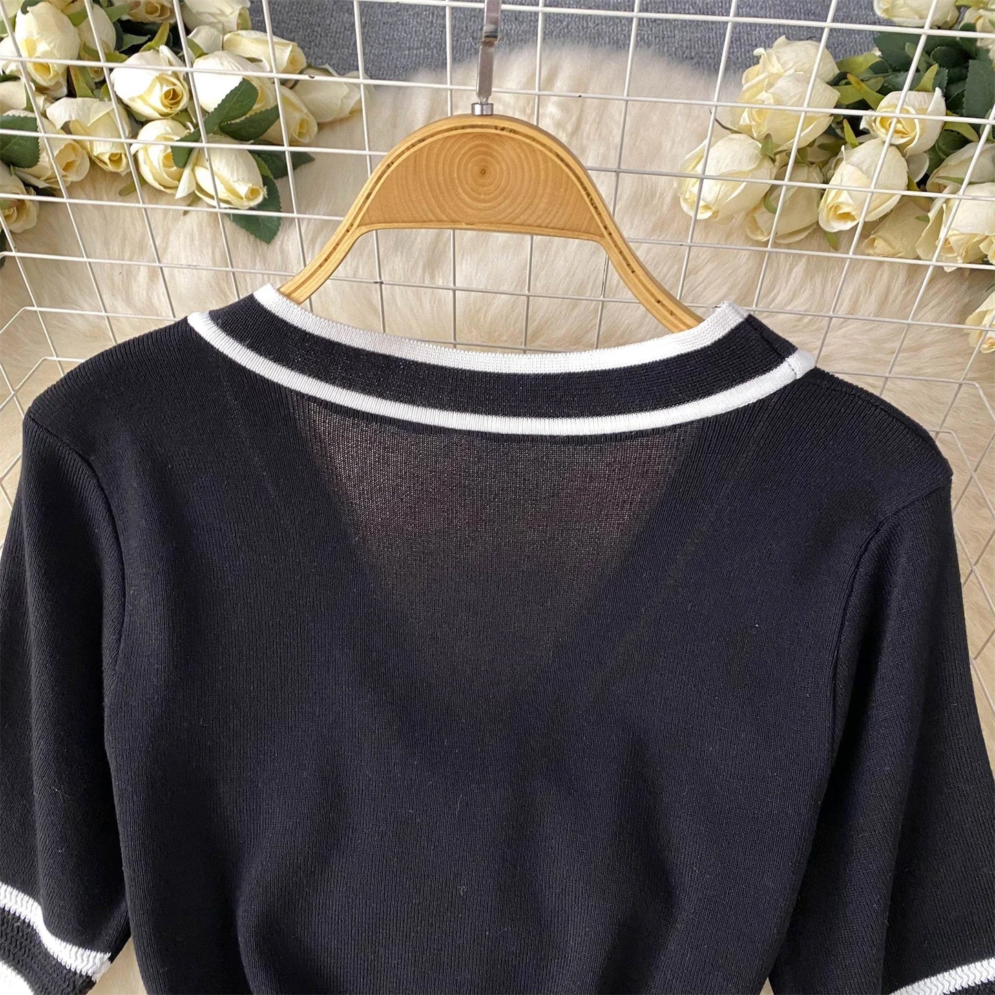 Black sweater with White trim on a wooden hanger against a floral and grid-patterned background