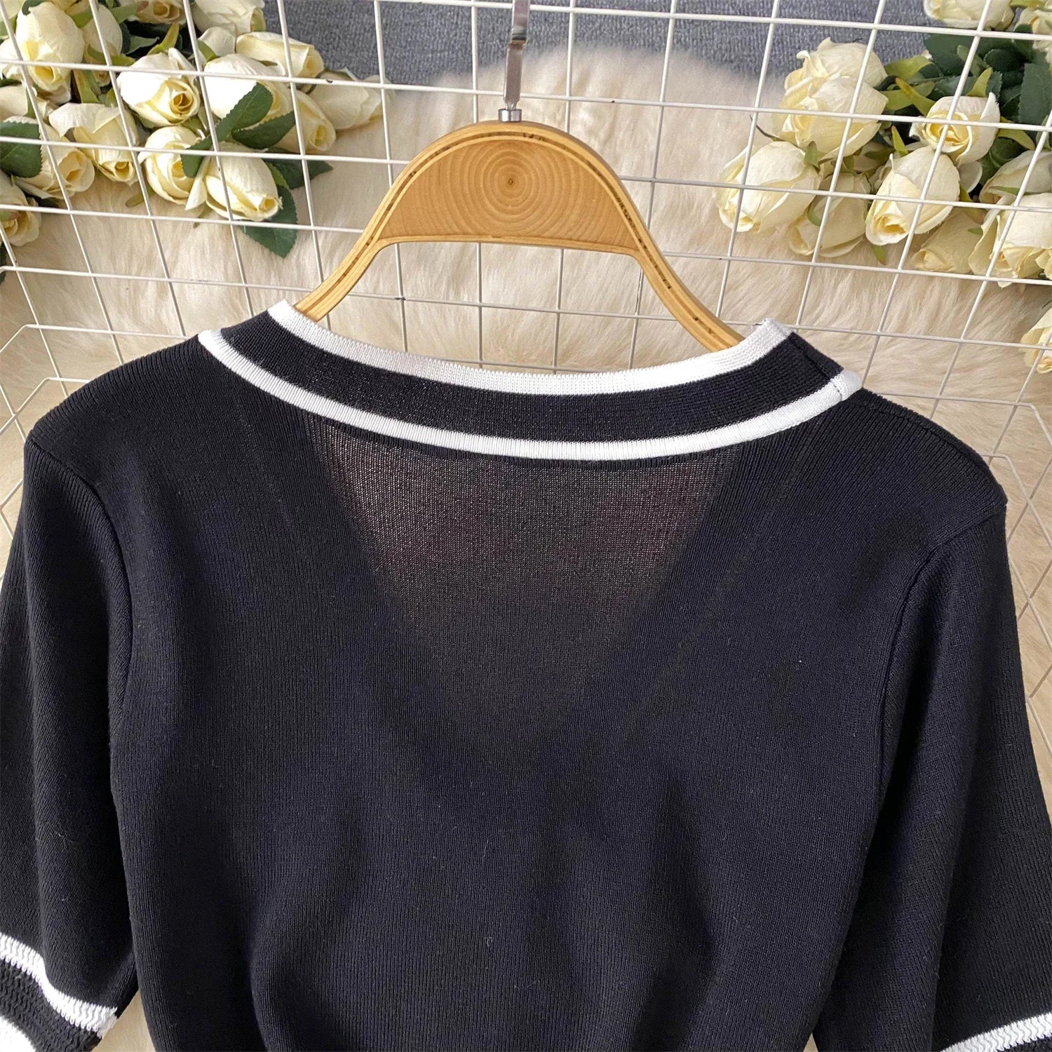 Black sweater with White trim on a wooden hanger against a floral and grid-patterned background