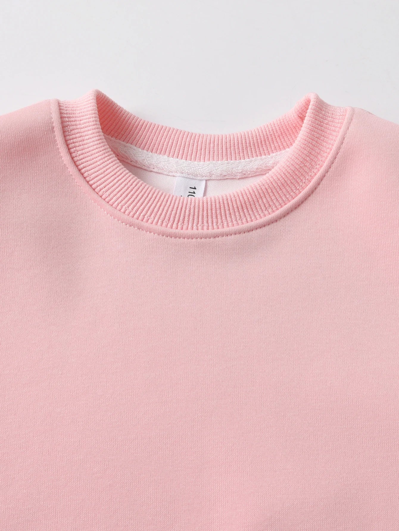 Close-up of a Pink sweater with a White label on a light Gray background