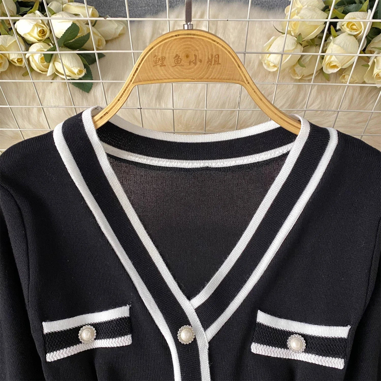 Black cardigan with White trim on a wooden hanger against a tiled wall background.