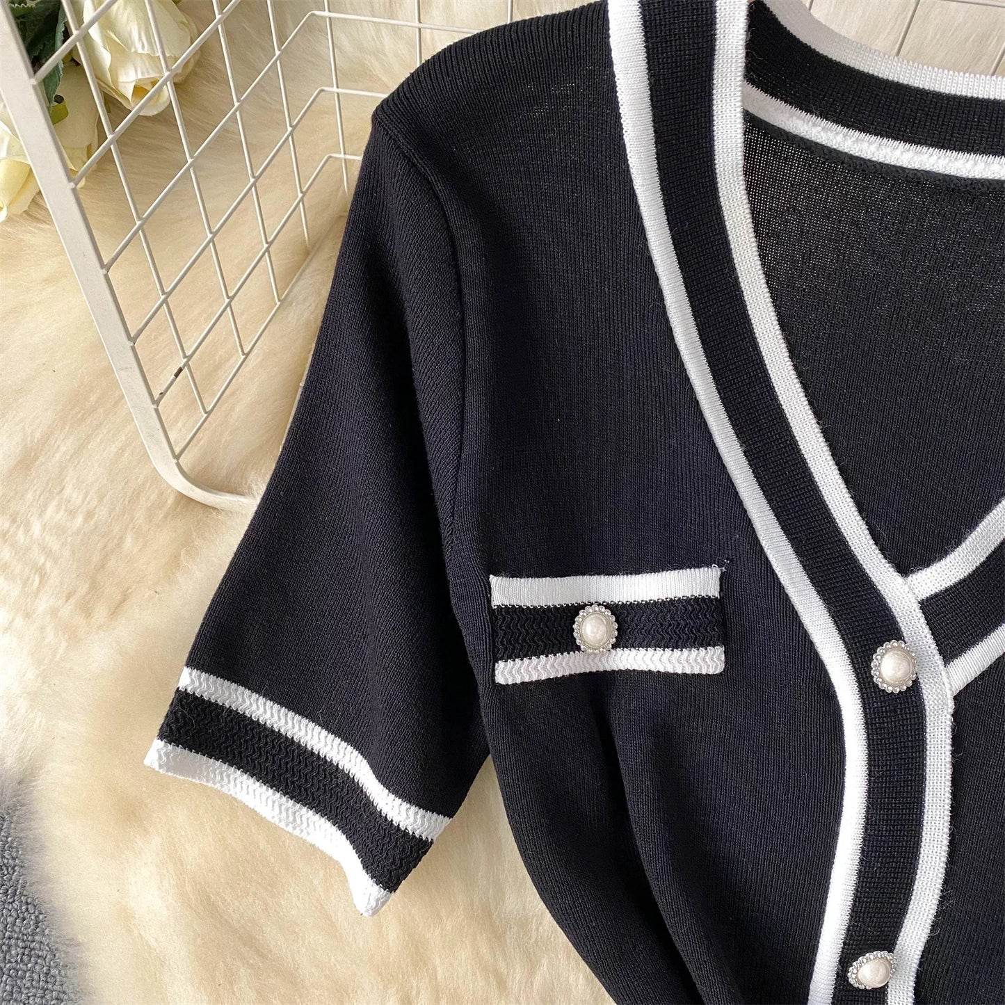 Black cardigan with White trim and buttons on a light wooden floor.