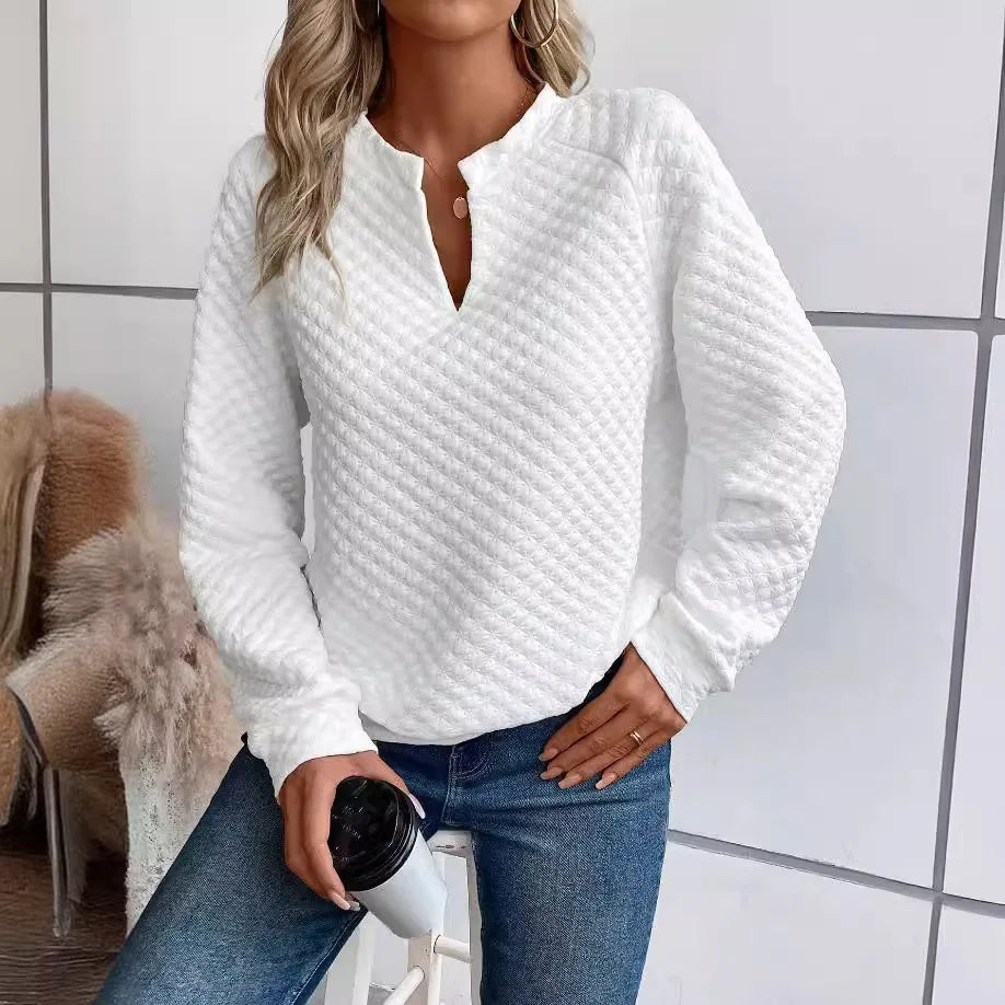 Person wearing a textuRed White long-sleeve top and Blue jeans, holding a coffee cup indoors.